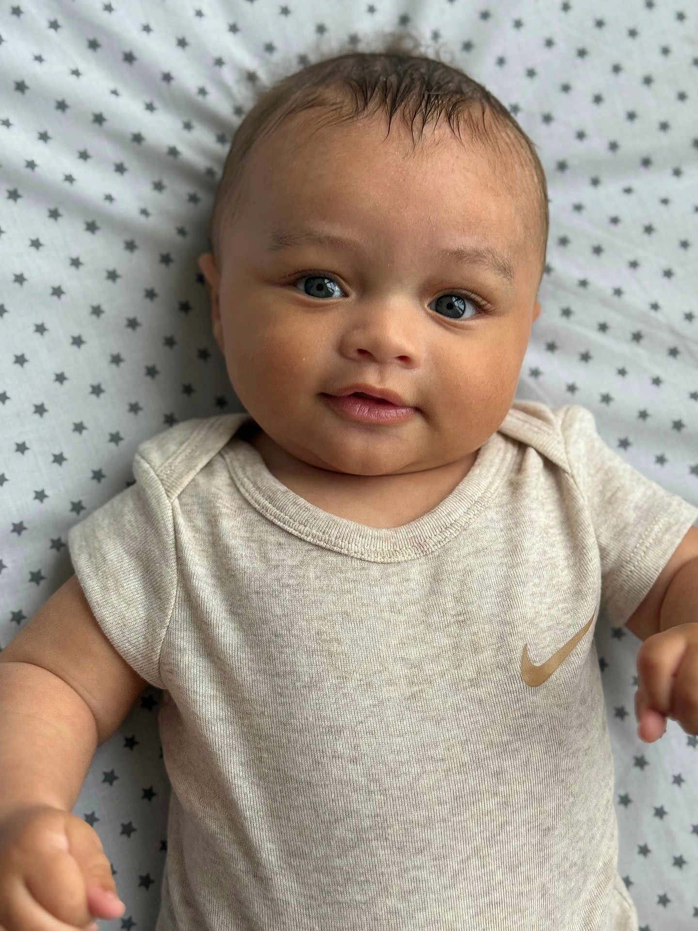 Jahyann a rejoint le concours — aidez-le/la à gagner de superbes lots ! baby, infant, child, face, eyes, clothing, onesie, nike_logo, blanket, pattern, stars, skin, cute, portrait, smile, hand, lying_down, soft_lighting, indoors, young