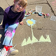 Khloey is registered to the contest to win money with this photo: art, casual_clothing, chalk, child, colorful, concrete, daytime, drawing, flower, hair, happy, outdoor, playful, red_socks, sidewalk, sitting, smiling, sneakers, sunny, young_girl