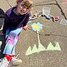Khloey is registered to the contest to win money with this photo: art, casual_clothing, chalk, child, colorful, concrete, daytime, drawing, flower, hair, happy, outdoor, playful, red_socks, sidewalk, sitting, smiling, sneakers, sunny, young_girl