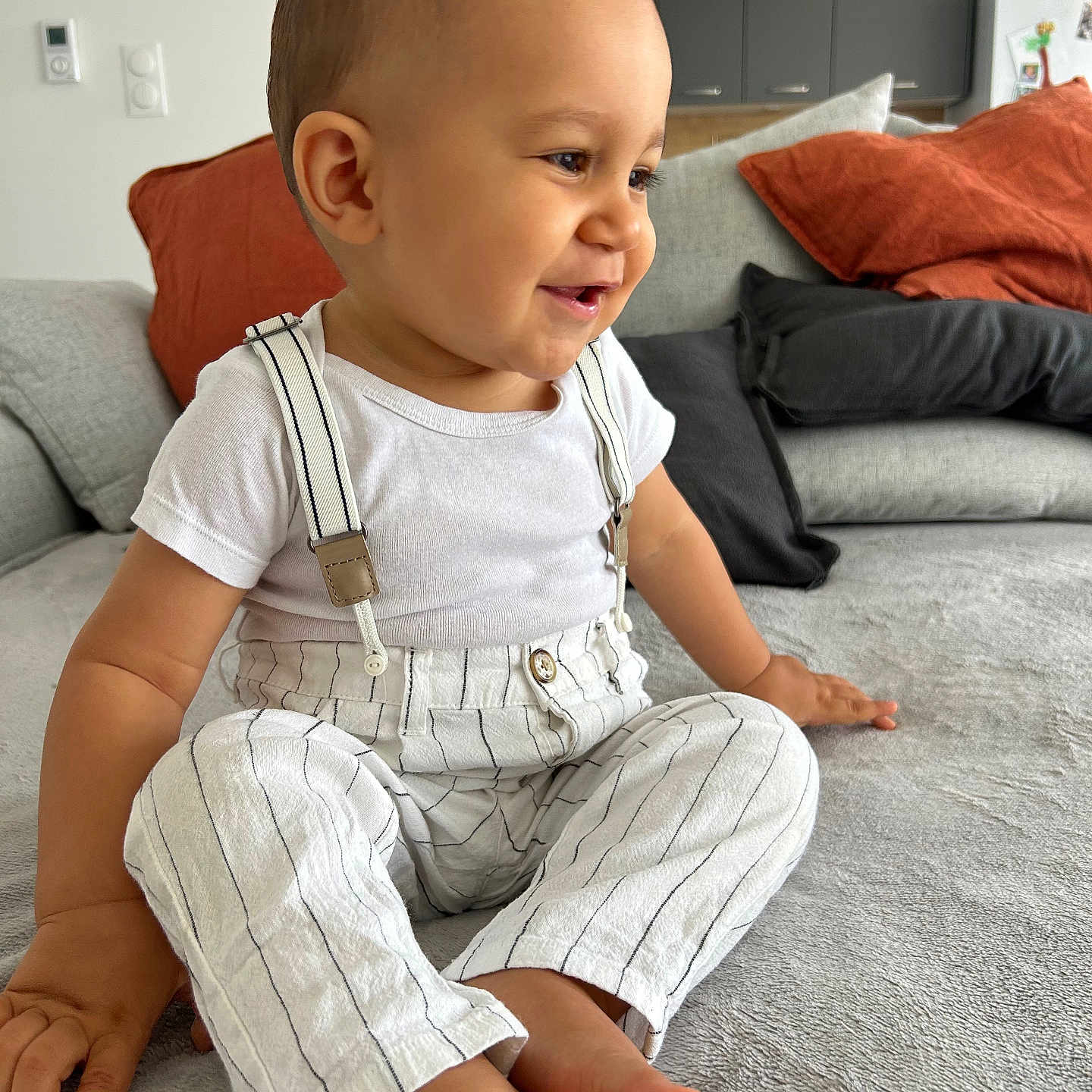 Siann participe au concours pour gagner de l'argent avec cette photo : barefoot, casual_clothing, child, couch, cute, face, happy, home, indoor, living_room, modern_interior, person, pillows, relaxed, sitting, smiling, striped_pants, suspenders, toddler, white_shirt