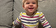 Camden is registered to the contest to win money with this photo: baby, child, smile, happy, sitting, couch, living_room, sweater, striped_clothing, gray_pants, white_socks, furniture, indoor, person, hair, face, expression, cozy, home, cute