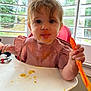 Camden joined the competition — help win amazing prizes! baby, child, high_chair, messy, food, spoon, face, bib, pink_clothing, curly_hair, indoor, window, greenery, table, feeding, cute, smile, toddler, hands, expression