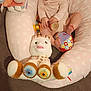 baby, infant, smiling, plush_toy, unicorn, giraffe, cushion, heart_pattern, wooden_toy, colorful, indoor, child, cute, happy, seated, soft_toys, fabric, person, playtime, cozy