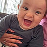 baby, smile, happy, child, infant, face, hand, clothing, person, indoor, curtains, holding, joy, cute, young, skin, eyes, cheeks, mouth, sitting