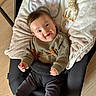 baby, infant, smiling, knitted_sweater, black_seat, blanket, giraffe_toy, socks, happy, baby_seat, wooden_floor, indoor, child, cute, playful, cozy, person, portrait, small_toy, relaxed