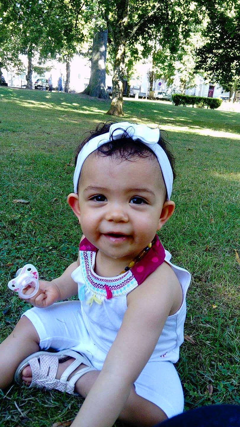 Léona participe au concours pour gagner de l'argent avec cette photo : child, day, facial_expression, fashion_accessory, fun, girl, grass, hair_accessory, happiness, head, headgear, infant, person, pink, plant, sitting, skin, smile, summer, toddler