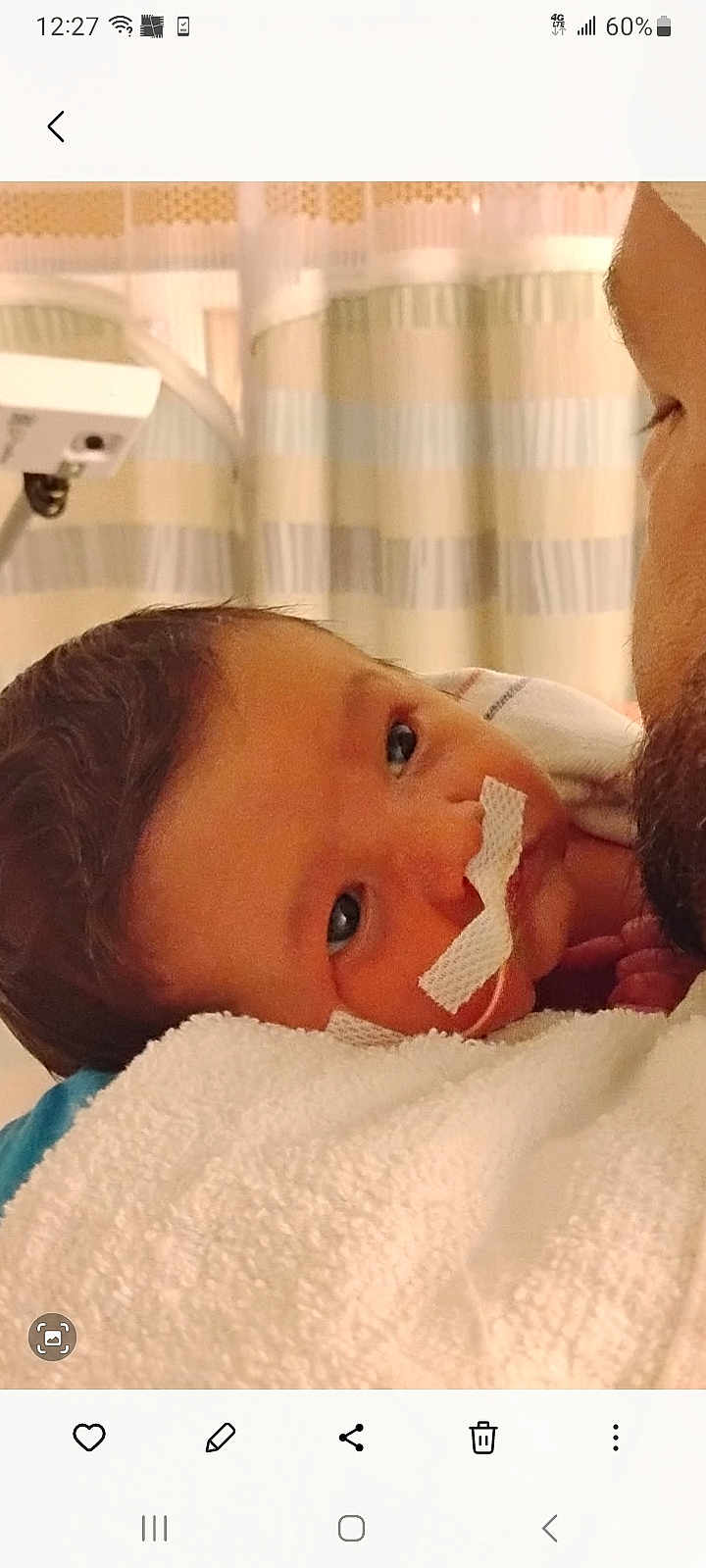 Elijah is registered to the contest to win money with this photo: baby, newborn, infant, hospital, nasal_tube, medical_tape, blanket, adult, holding, close_up, face, eyes, curtains, tender_moment, indoor, person, care, healthcare, wrap, rest