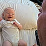 Luca is registered to the contest to win money with this photo: baby, smile, person, bed, pillow, white_clothing, remote_control, hand_holding, indoor, furniture, chair, clothing, tattoo, skin, face, head, legs, adult, infant, happy