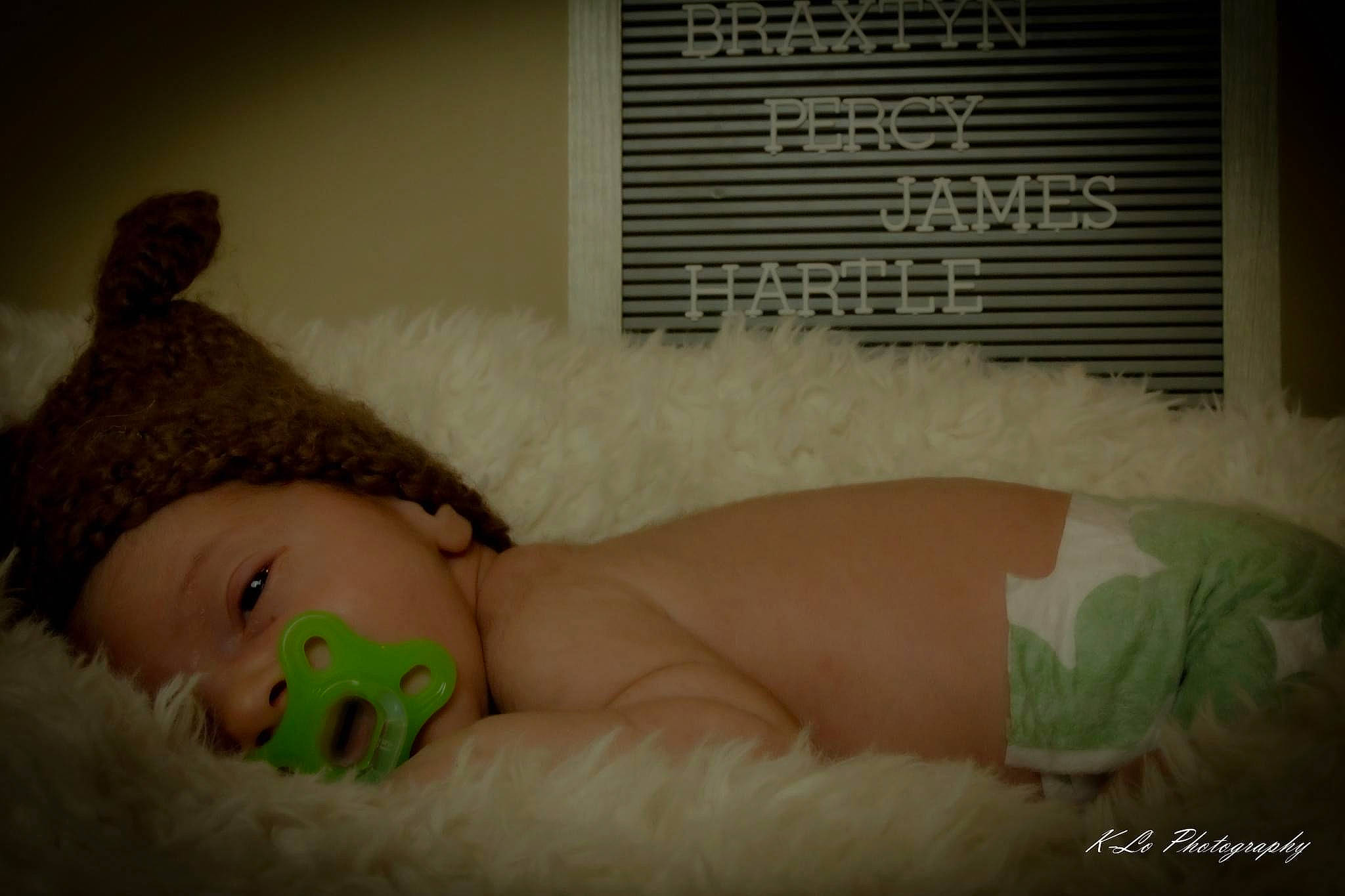 Braxtyn is registered to the contest to win money with this photo: arm, black_hair, cap, child, comfort, eye, eyebrow, eyelash, fur, grass, hair, hair_accessory, hand, happy, head, headpiece, human_body, human_leg, linens, person