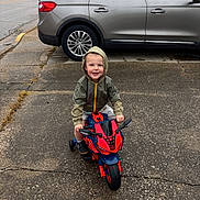 Ikaris joined the competition — help win amazing prizes! car, casual_clothing, child, daytime, happy, hood, hooded_jacket, outdoor, pavement, person, play, sidewalk, small_bike, smiling, street, toddler, toy_motorcycle, transportation, urban, vehicle