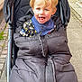 Dylan is registered to the contest to win money with this photo: toddler, child, stroller, outdoor, sidewalk, bicycle, car, blonde_hair, happy, winter_clothing, jacket, urban, pavement, baby_bib, playful, expression, transport, person, daylight, city