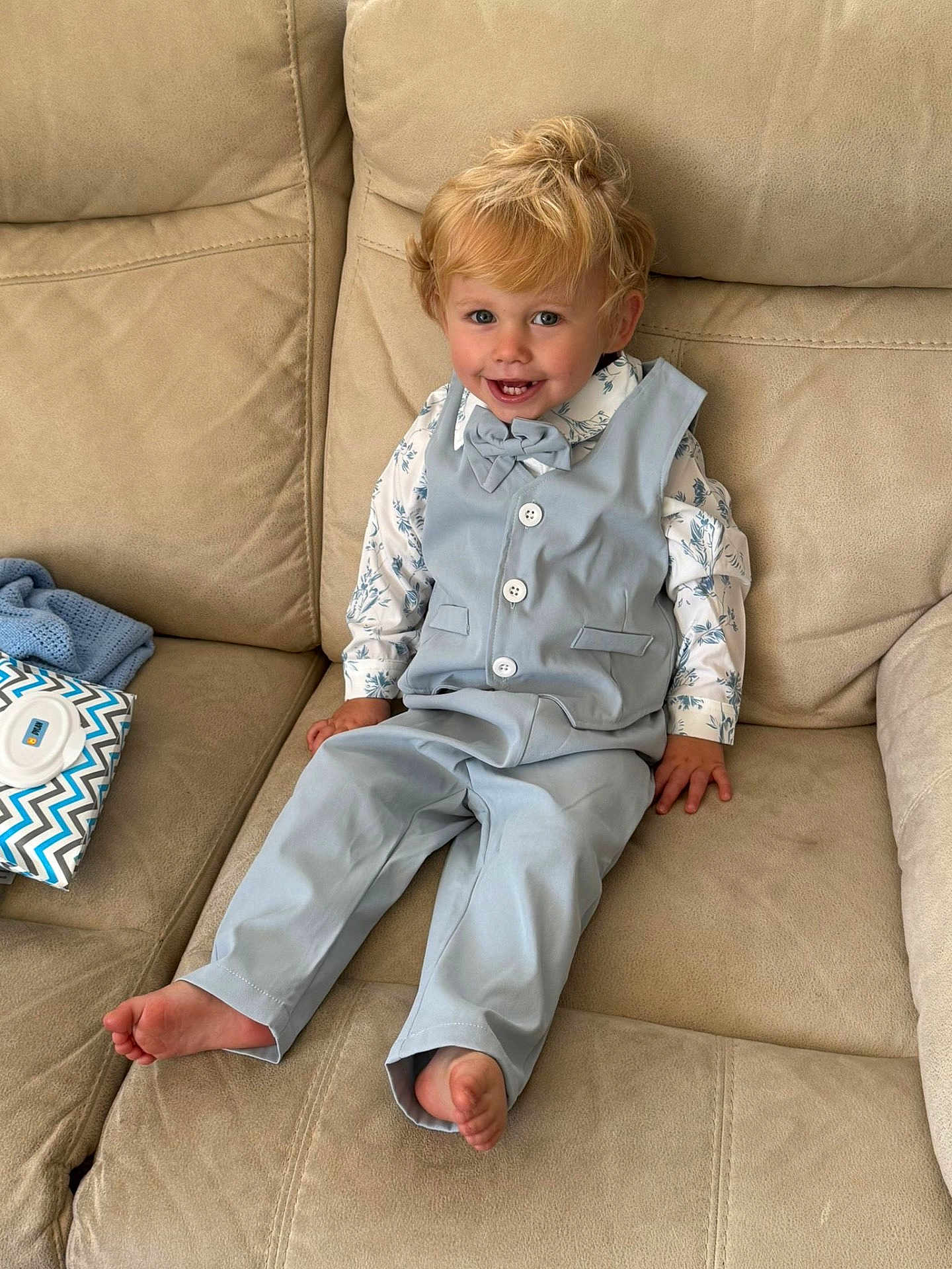 Dylan is registered to the contest to win money with this photo: toddler, child, smiling, suit, bow_tie, couch, beige, blond_hair, barefoot, indoor, happy, portrait, seated, fabric, buttons, baby_wipes, pattern, furniture, casual, cute