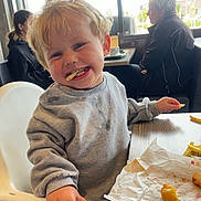 Dylan joined the competition — help win amazing prizes! toddler, child, high_chair, food, french_fries, fried_food, restaurant, indoor, casual, messy_face, smiling, blond_hair, sweatshirt, table, window, lamp, people, seated, daylight, hand