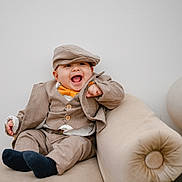 Jairo joined the competition — help win amazing prizes! baby, child, smiling, laughing, suit, bow_tie, hat, cap, beige, couch, balloons, indoor, cute, happy, portrait, fashion, toddler, clothing, furniture, celebration