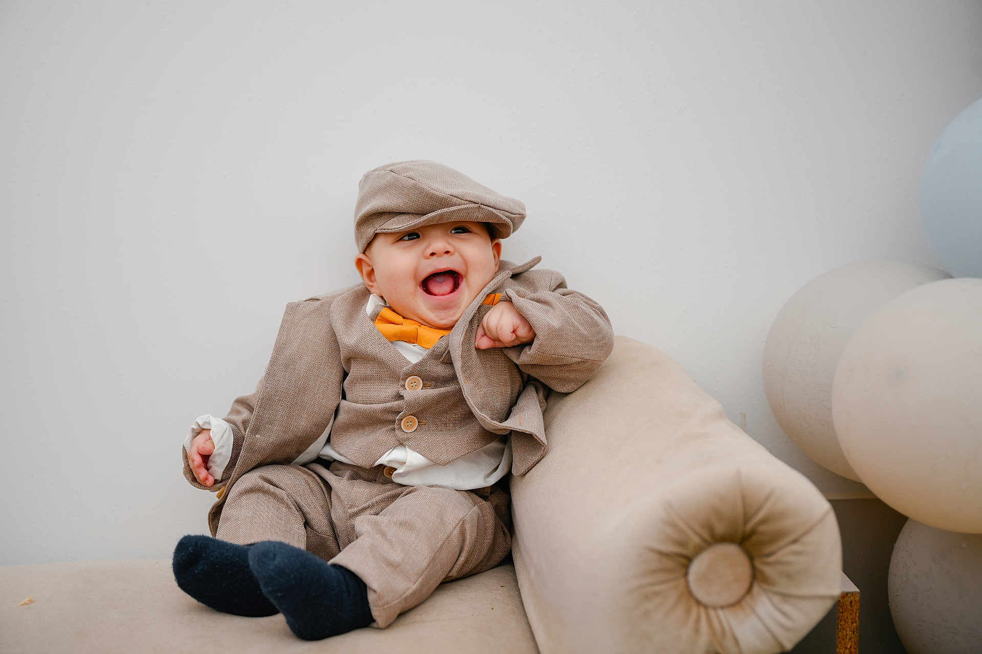 Jairo joined the competition — help win amazing prizes! baby, child, smiling, laughing, suit, bow_tie, hat, cap, beige, couch, balloons, indoor, cute, happy, portrait, fashion, toddler, clothing, furniture, celebration