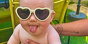 Lexie a rejoint le concours — aidez-le/la à gagner de superbes lots ! baby, sunglasses, heart_shaped, tongue_out, diaper, tattoo, adult_hand, outdoor, greenery, table, chair, baby_bottle, summer, funny_face, cute, child, person, playful, sunlight, casual