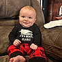 Bo is registered to the contest to win money with this photo: baby, smiling, infant, sitting, red_plaid_pants, black_shirt, indoor, couch, furniture, foot, hand, face, cute, child, home, cozy, portrait, expression, comfort, clothing