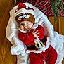 Bo is registered to the contest to win money with this photo: baby, child, infant, christmas, holiday, festive, red_clothing, hat, reindeer_hat, blanket, wooden_floor, tree, pine_branches, cute, smiling, indoors, cozy, fur_trim, person, foot