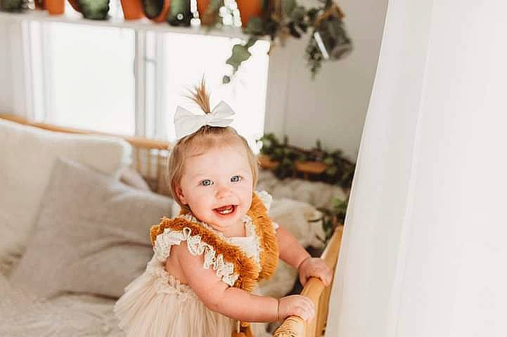 Caylee is registered to the contest to win money with this photo: baby, baby_toddler_clothing, child, couch, event, fashion_accessory, flash_photography, formal_wear, hair_accessory, happy, headband, headpiece, jewellery, joy, pattern, peach, person, picture_frame, room, smile