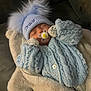Draco is registered to the contest to win money with this photo: baby, sleeping, pacifier, hat, knitted_sweater, blue_clothing, pom_poms, blanket, couch, cozy, indoor, child, cute, soft_texture, resting, warm_clothing, portrait, infant, handwear, personalized