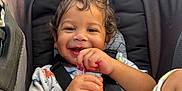 Takoah is registered to the contest to win money with this photo: toddler, child, smile, curly_hair, car_seat, seatbelt, snack, happy, cute, infant, clothing, baby, hands, face, sitting, indoor, young_child, cozy, playful, joy