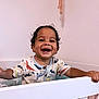 toddler, child, smiling, laughing, crib, baby, indoor, clothing, dinosaur_pattern, happy, portrait, face, hand, young_child, room, furniture, cute, curly_hair, skin, buttoned_shirt