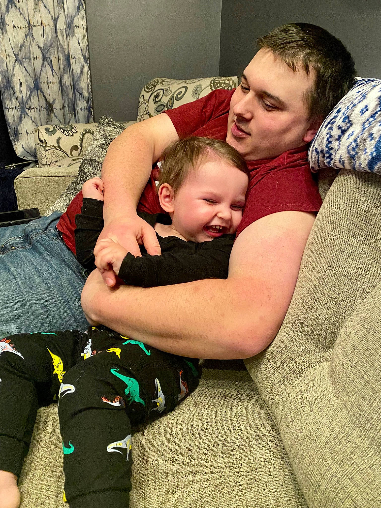 Timothy is registered to the contest to win money with this photo: baby, child, comfort, couch, curtain, elbow, fun, grass, hairstyle, happy, houseplant, human_leg, joint, knee, lap, person, plant, sitting, t_shirt, thigh