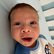 Ezekiel is registered to the contest to win money with this photo: baby, child, face, smiling, blue_clothing, mickey_mouse, pattern, striped_background, infant, cute, portrait, happy, lying_down, soft_surface, short_hair, indoors, close_up, person, toddler, apparel