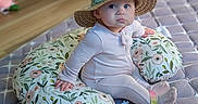Winslette is registered to the contest to win money with this photo: baby, child, cute, floor, floral_pattern, hat, home, indoor, infant, nursery, onesie, pacifier_clip, pillow, quilted_mat, sitting, sock, soft_lighting, straw_hat, wide_eyes, wooden_floor
