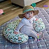baby, child, cute, floor, floral_pattern, hat, home, indoor, infant, nursery, onesie, pacifier_clip, pillow, quilted_mat, sitting, sock, soft_lighting, straw_hat, wide_eyes, wooden_floor