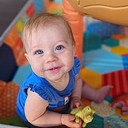 Alice is registered to the contest to win money with this photo: baby, child, blue_eyes, toy, dinosaur_toy, playpen, colorful, smiling, sitting, infant, cute, happy, indoor, clothing, blue_shirt, person, young_child, play, hand, face
