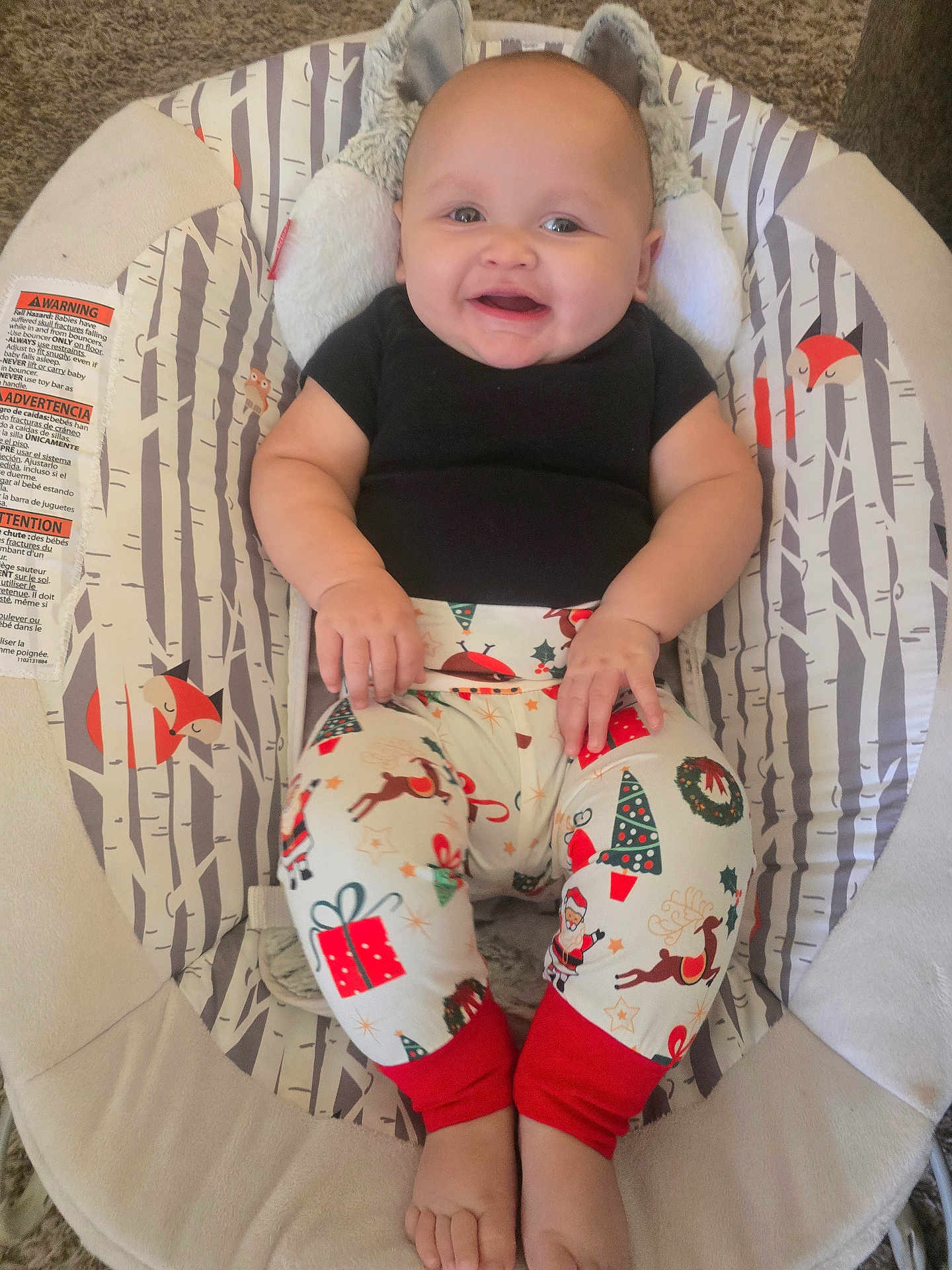 Grayson is registered to the contest to win money with this photo: baby, child, smiling, sitting, black_shirt, christmas_pants, holiday_theme, baby_chair, woodland_pattern, fox_pattern, indoor, happy, cute, infant, feet, hands, head, face, plush, carpet