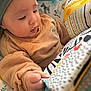 baby, child, infant, sweater, headband, soft_toy, book, patterned, animal_prints, hand, curious, close_up, indoor, cozy, childhood, playtime, colorful, fabric, young, portrait