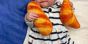 Aoife joined the competition — help win amazing prizes! baby, infant, striped_clothing, hat, plush_toy, bread_toy, croissant_toy, soft_surface, blue_background, white_background, cute, child, lying_down, adorable, smiling, indoor, person, cozy, fashion, portrait