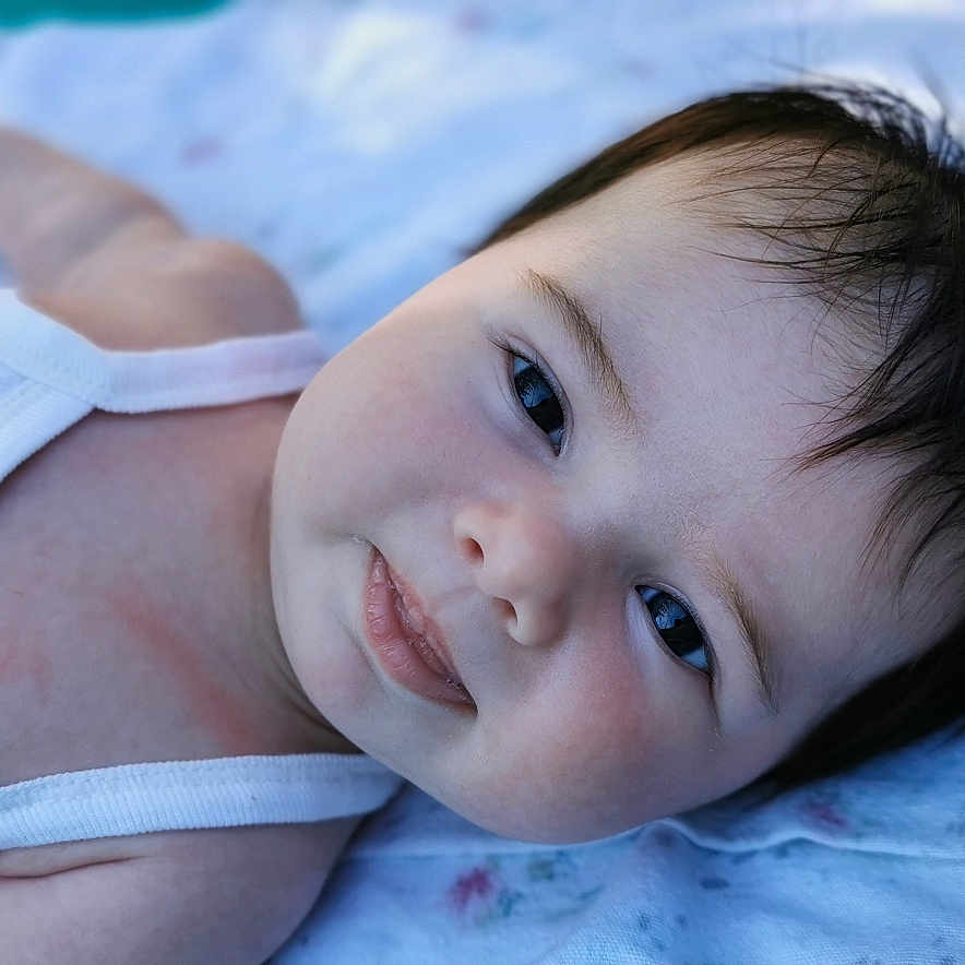 Elicia participe au concours pour gagner de l'argent avec cette photo : baby, blanket, cheeks, child, closeup, clothing, cute, eyes, face, hair, indoors, infant, lying_down, onesie, person, portrait, skin, smile, soft_light, young