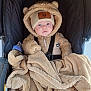 Kai is registered to the contest to win money with this photo: baby, child, stroller, blanket, hat, beige, fur, warm_clothing, cute, face, blue_eyes, bundle, infant, cozy, teddy_bear, outdoor, winter, person, seatbelt, clothing