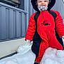 Diego participe au concours pour gagner de l'argent avec cette photo : child, toddler, snow, winter_clothing, red_coat, hood, beanie, gloves, smile, happy, snowbank, building, metal_siding, outdoor, cold_weather, boots, playful, face, portrait, jacket
