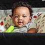 baby, child, curly_hair, striped_shirt, toy, green_toy, baby_seat, patterned_cushion, indoor, smiling, happy, face, portrait, infant, cute, childrens_toy, closeup, person, sitting, young_child