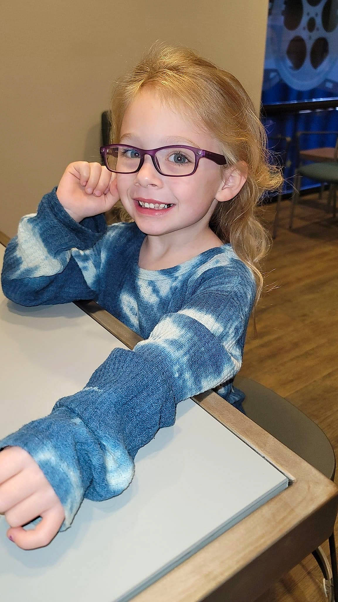 Paisley is registered to the contest to win money with this photo: blue, chair, cheek, chin, eye, facial_expression, finger, gesture, glasses, hair, hairstyle, head, iris, joy, organ, person, purple, sleeve, smile, standing