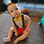 baby, child, sitting, carpet, yellow_bow_tie, polka_dot_suspender, headband, black_ears, indoors, cute, curious, bare_chest, red_shorts, infant, floor, person, toddler, expression, playful, young_child