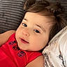 toddler, child, curly_hair, red_clothing, ladybug_print, face, smiling, indoor, couch, pillow, closeup, portrait, relaxed, baby, skin, person, soft_texture, cozy, young_child, casual