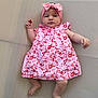 baby, infant, child, pink_dress, headband, floral_pattern, barefoot, lying_down, textured_surface, cute, portrait, skin, hand, foot, face, young_child, clothing, fashion, indoors, expression