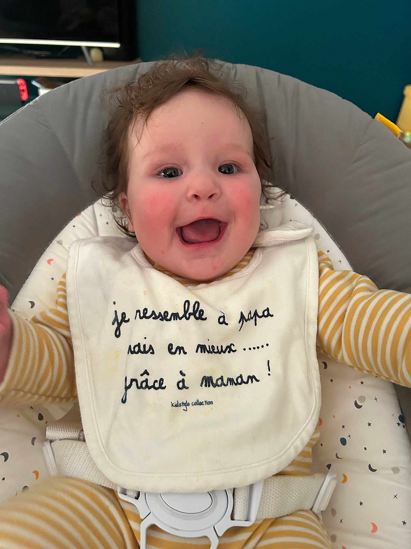 Jade participe au concours pour gagner de l'argent avec cette photo : baby, child, smiling, happy, indoor, curly_hair, bib, striped_clothing, seat, cushion, face, person, infant, closeup, cheeks, cute, playful, comfortable, expression, joy