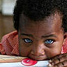 Jason is registered to the contest to win money with this photo: child, toddler, baby, portrait, face, eyes, blue_eyes, curious, serious, looking_at_camera, hands, table, buttons, colorful, indoor, close_up, head, hair, red_clothing, photograph