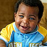 Jason is registered to the contest to win money with this photo: baby, child, infant, smiling, portrait, face, eyes, curly_hair, blue_eyes, colorful_clothing, sportswear, blue, yellow, collar, button, indoors, close_up, sitting, happy, photograph