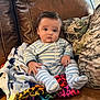Brenden is registered to the contest to win money with this photo: baby, infant, child, striped_pajamas, blanket, leather_sofa, pillow, cushion, living_room, sitting, portrait, wide_eyes, chubby_cheeks, hands, feet, fuzzy_blanket, home_interior, cozy, soft_light, cute