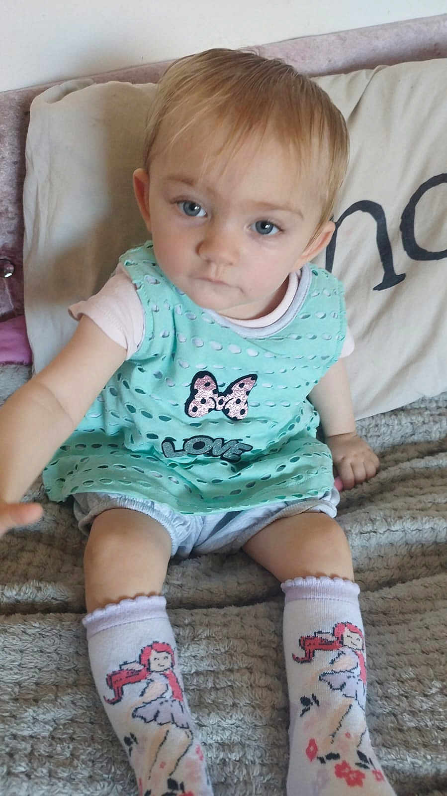 Keisha is registered to the contest to win money with this photo: toddler, child, baby, sitting, reaching, blue_eyes, mint_green_dress, butterfly, love_text, socks, cartoon_socks, blanket, indoor, cute, portrait, curious, young_child, light_hair, cozy, soft_texture