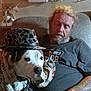 Sparky is registered to the contest to win money with this photo: man, dog, blanket, hat, indoor, chair, sleeping, beard, tattoo, leopard_print, casual, relaxing, pet, animal, human, tshirt, seated, resting, furniture, cozy