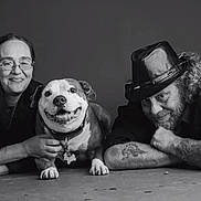 Sparky joined the competition — help win amazing prizes! black_and_white, dog, smiling, people, portrait, happy, man, woman, tattoo, hat, glasses, floor, lying_down, collar, pet, casual, friendly, indoor, adult, relaxed