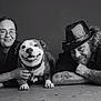black_and_white, dog, smiling, people, portrait, happy, man, woman, tattoo, hat, glasses, floor, lying_down, collar, pet, casual, friendly, indoor, adult, relaxed